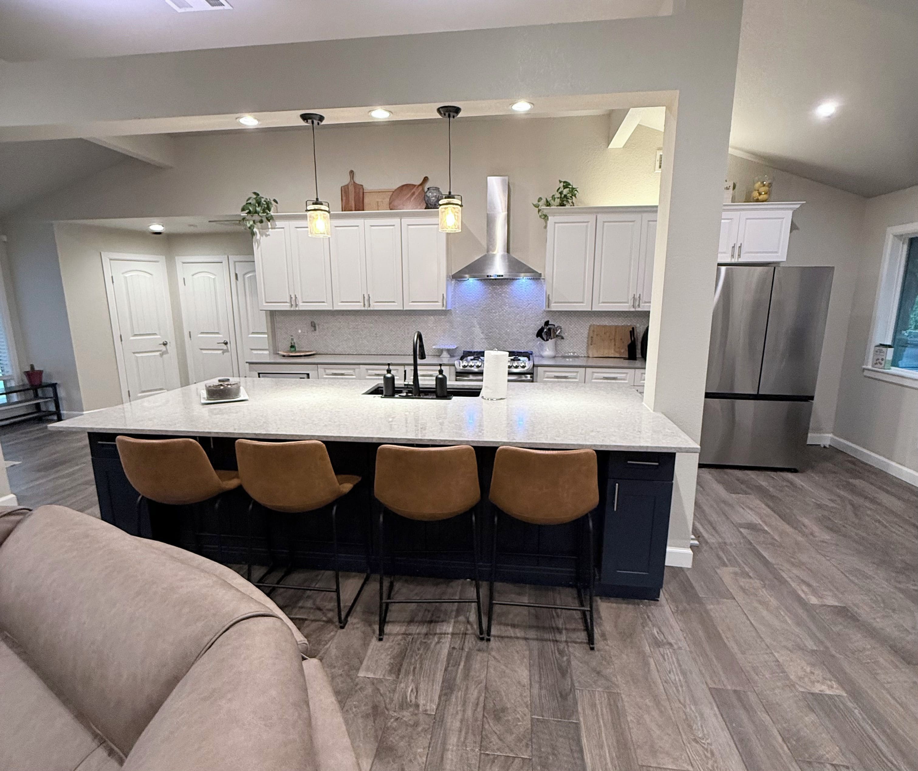 Una cocina moderna con una isla grande, taburetes de bar, electrodomésticos de acero inoxidable e iluminación colgante.