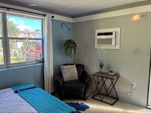 A room with a bed, a chair, a small table, a hanging plant, and an air conditioning unit. - Charming studio in Hollywood with fabulous kitchen (Hollywood)