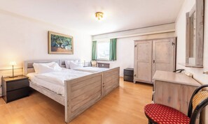 Ein Schlafzimmer mit einem Doppelbett, einem Nachttisch, einem Sessel, einem Kleiderschrank und einem Fenster mit Vorhängen.