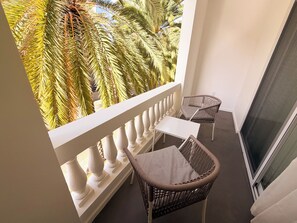 A balcony with two wicker chairs and a small table, overlooking palm trees. - King Suite Downtown Walk 2 Beach CasaAmarilla204 (Oranjestad)