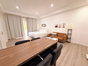 A modern hotel room with a wooden dining table, a sofa, a bed, and a nightstand. - King Suite Downtown Walk 2 Beach CasaAmarilla204 (Oranjestad)