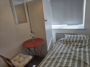 Et lille rum med en seng, en stol, et bord med en vase og et vindue.