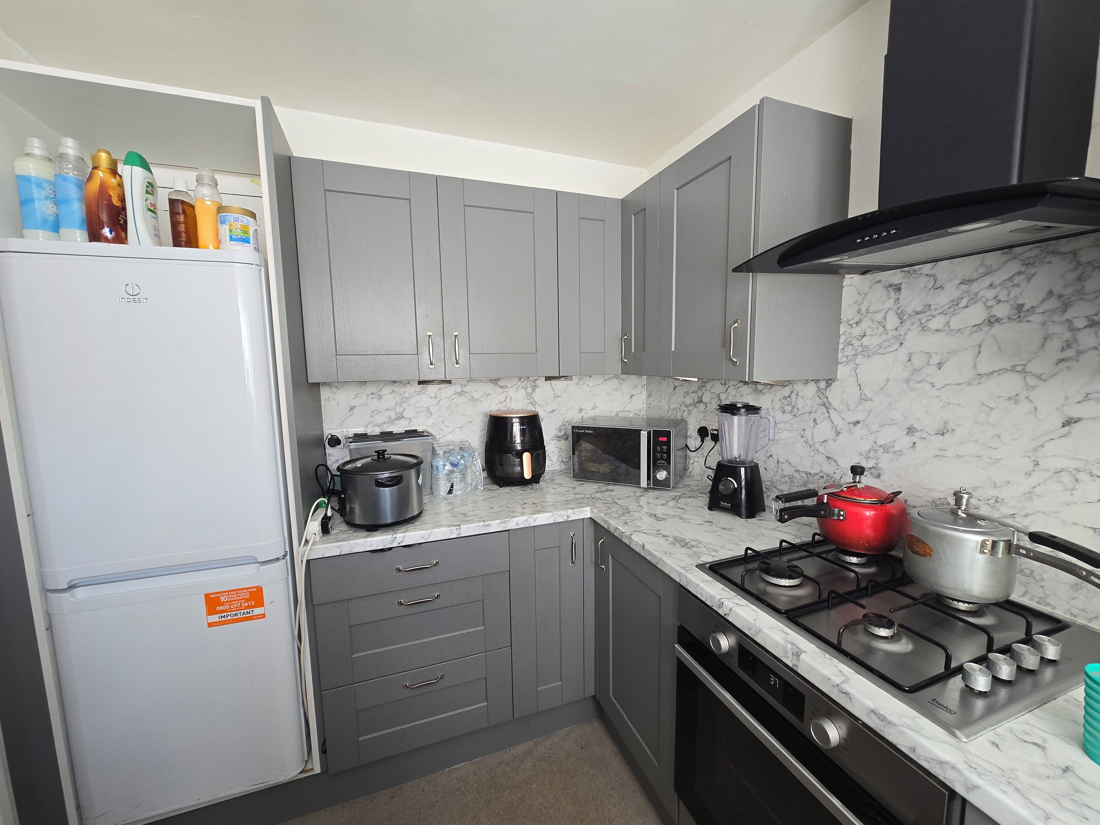 A compact kitchen with grey cabinets, a white refrigerator, a gas stove, a microwave, a toaster, and a blender.