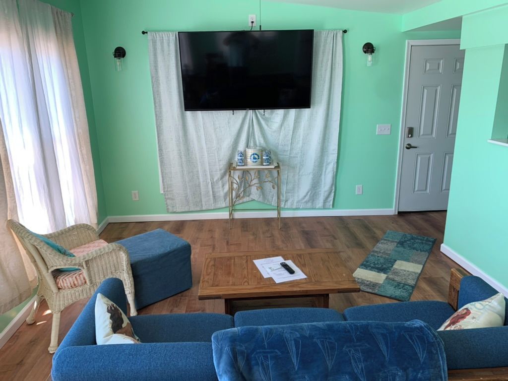 Una sala de estar con un juego de sofá, una mesa de centro, un televisor montado en la pared y una puerta al fondo.