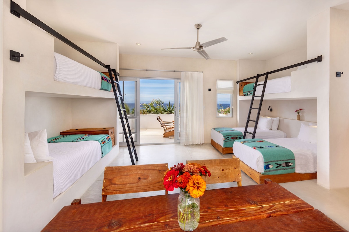 Habitación de hotel moderna con literas, una mesa de madera con un florero y un balcón con vistas.