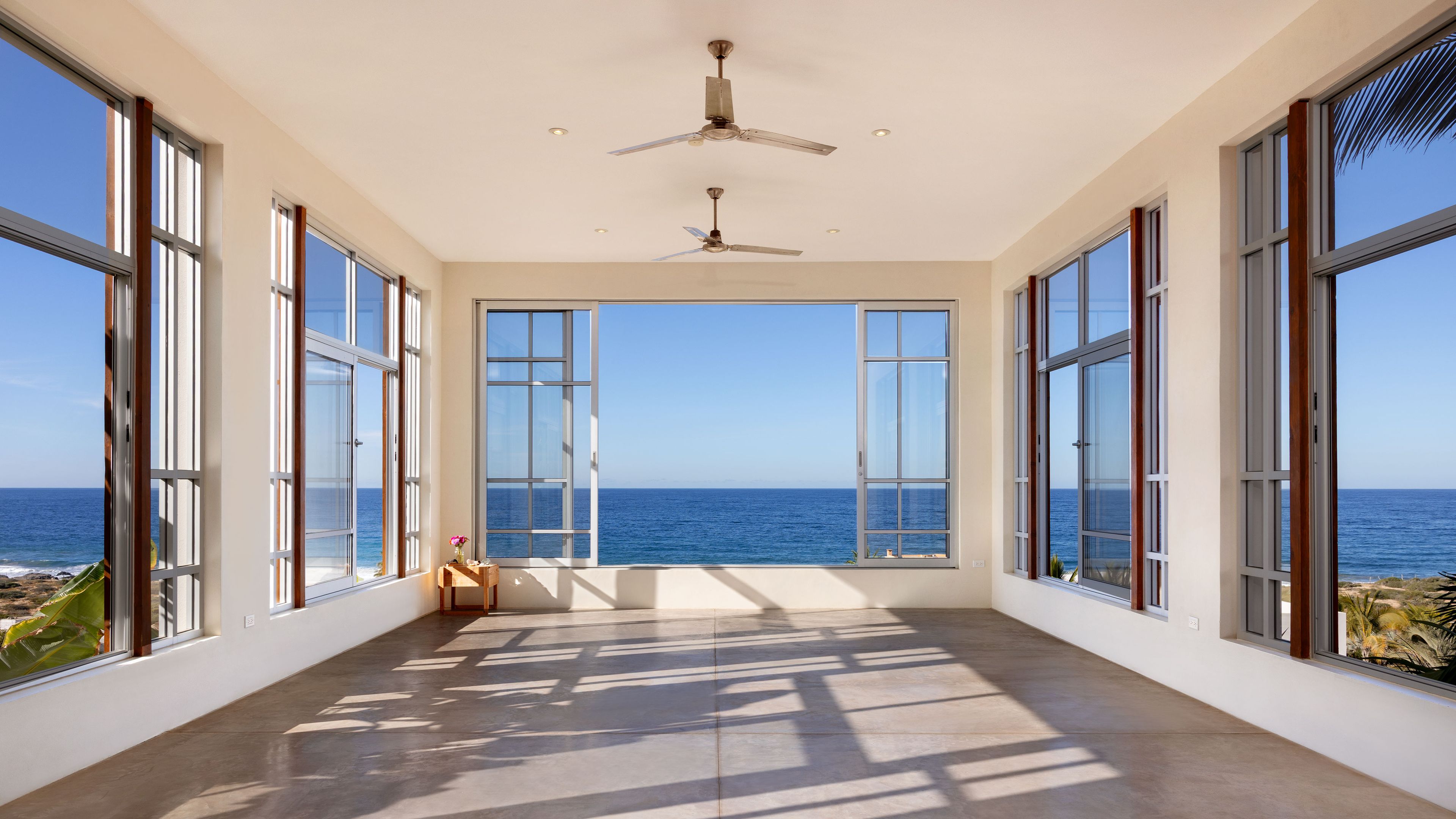 Una habitación con ventanas amplias, ventilador de techo y vista al océano.