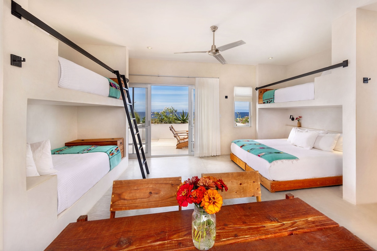Ein modernes Schlafzimmer mit Etagenbetten, einem Holztisch mit Blumenvase und einem Balkon mit Blick.