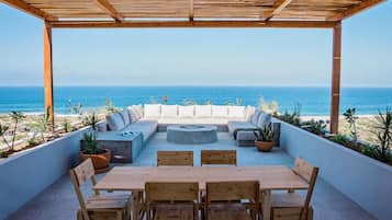 Een buitenpatio met een houten pergola, een zithoek met kussens, een ronde tafel en stoelen.
