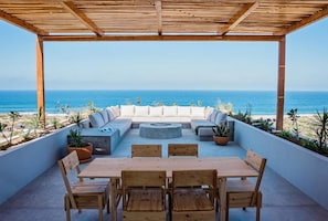 Eine Außenpatio mit einer Holzpergola, einer Sitzecke mit Kissen, einem runden Tisch und Stühlen.
