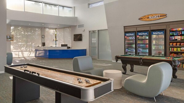Een pooltafel, stoelen, een receptiebalie en een automatenhoek in de hotellobby.