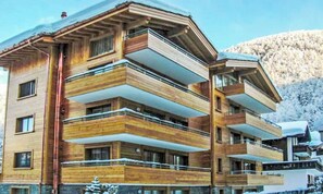 A multi-story hotel with balconies, wooden facade, and a mountainous backdrop. - SPACIOUS MOUNTAIN APARTMENT WITH LARGE SOUTH-FACING BALCONY (Zermatt)