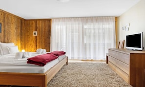 A bedroom with a bed, a wooden headboard, a TV on a wooden dresser, and a window with sheer curtains. - SPACIOUS MOUNTAIN APARTMENT WITH LARGE SOUTH-FACING BALCONY (Zermatt)