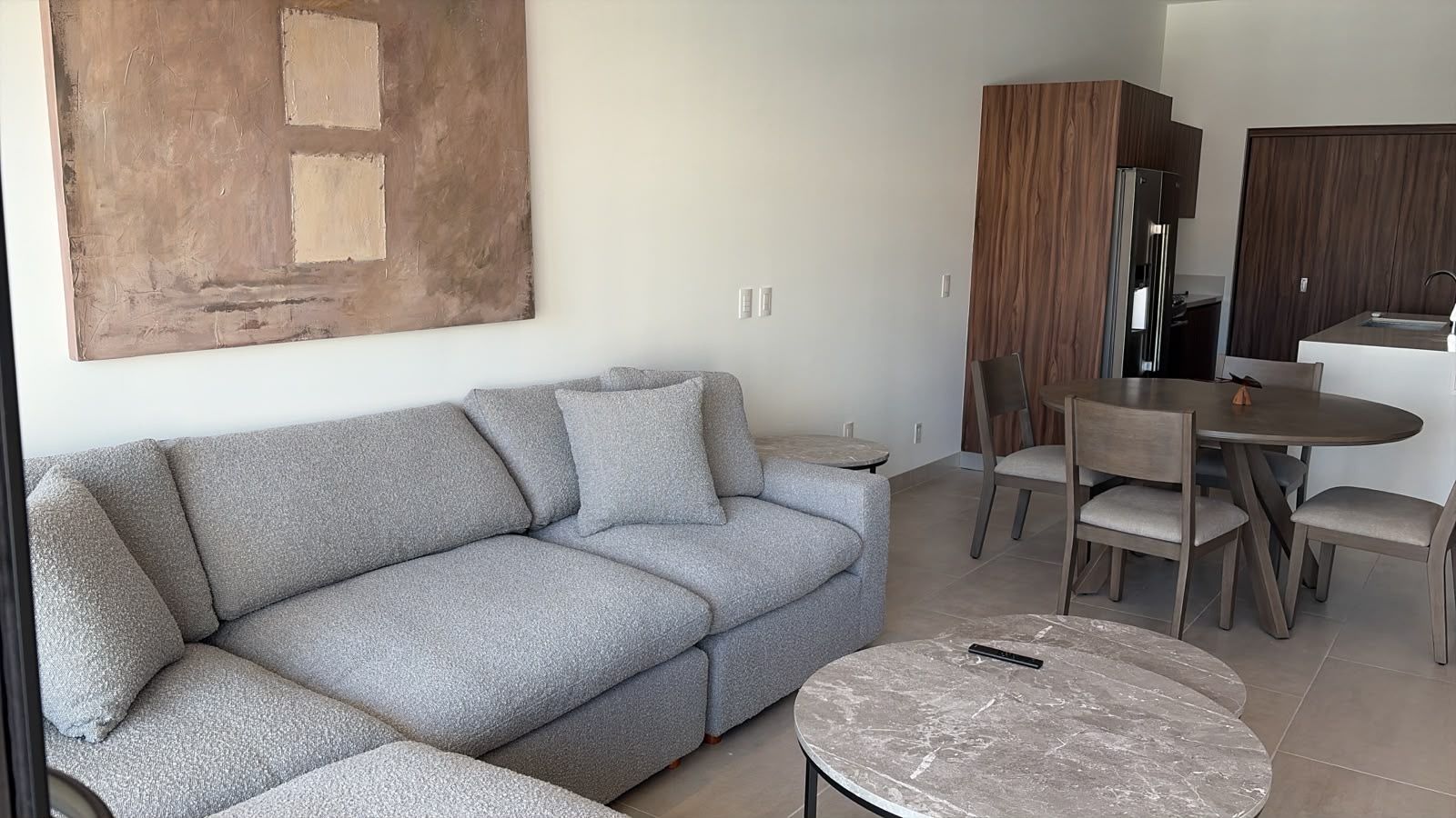 A modern living room with a grey sofa, a round coffee table, and a dining area with chairs and a table.