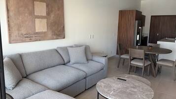 A modern living room with a grey sofa, a round coffee table, and a dining area with chairs and a table.