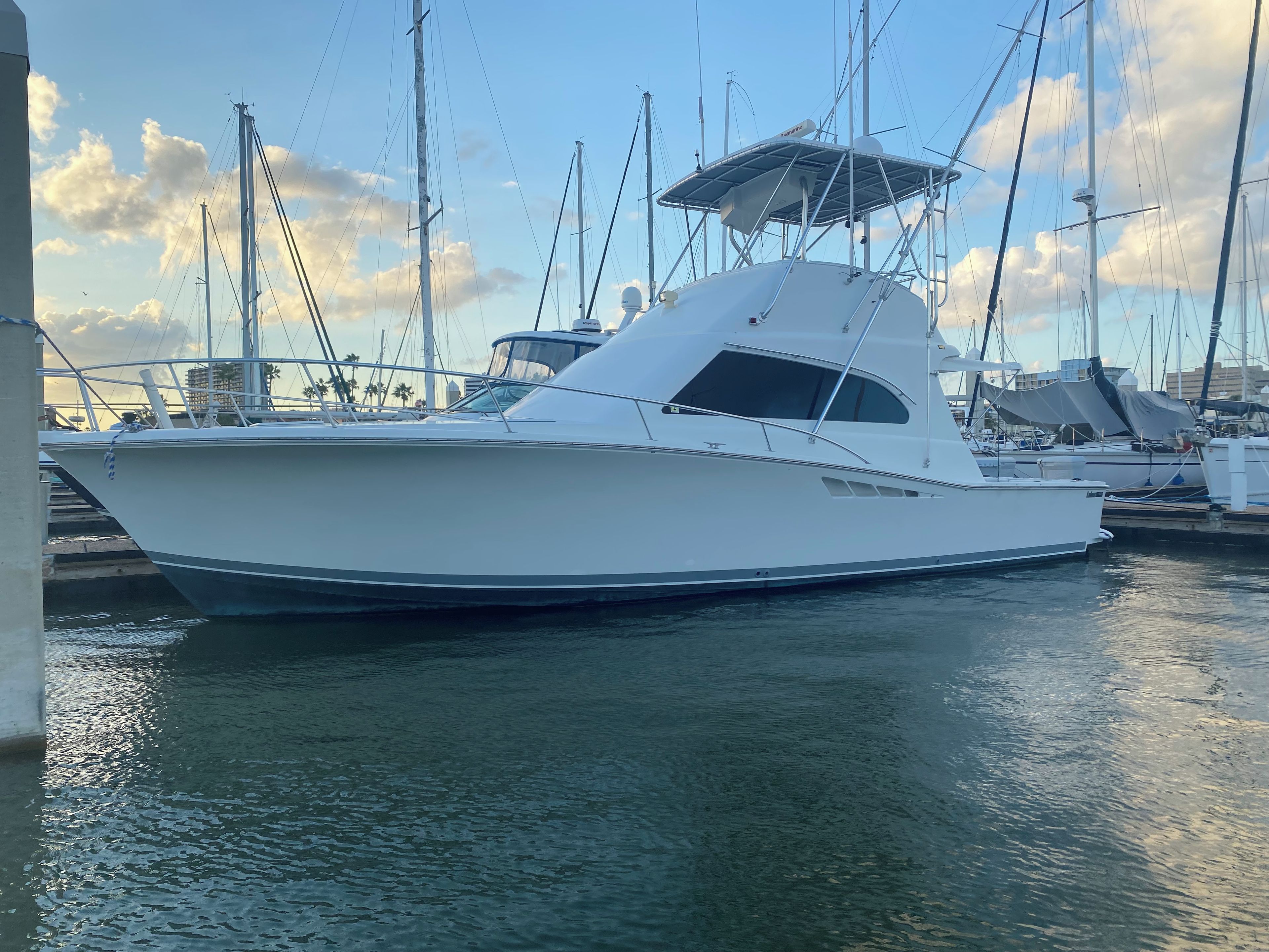 A white yacht docked at a marina with other boats and a clear sky in the background.