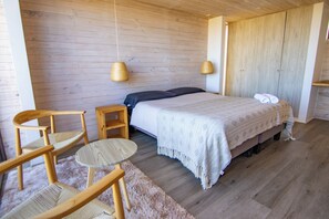 Un dormitorio con cama, dos sillas, una mesita y suelo de madera.