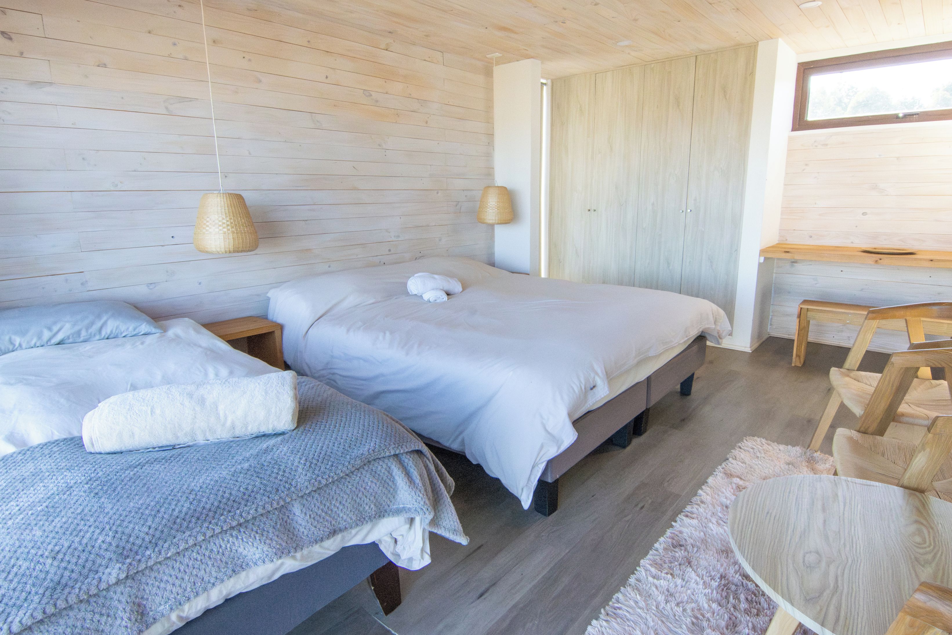 A bedroom with two beds, a wooden desk, and a window.