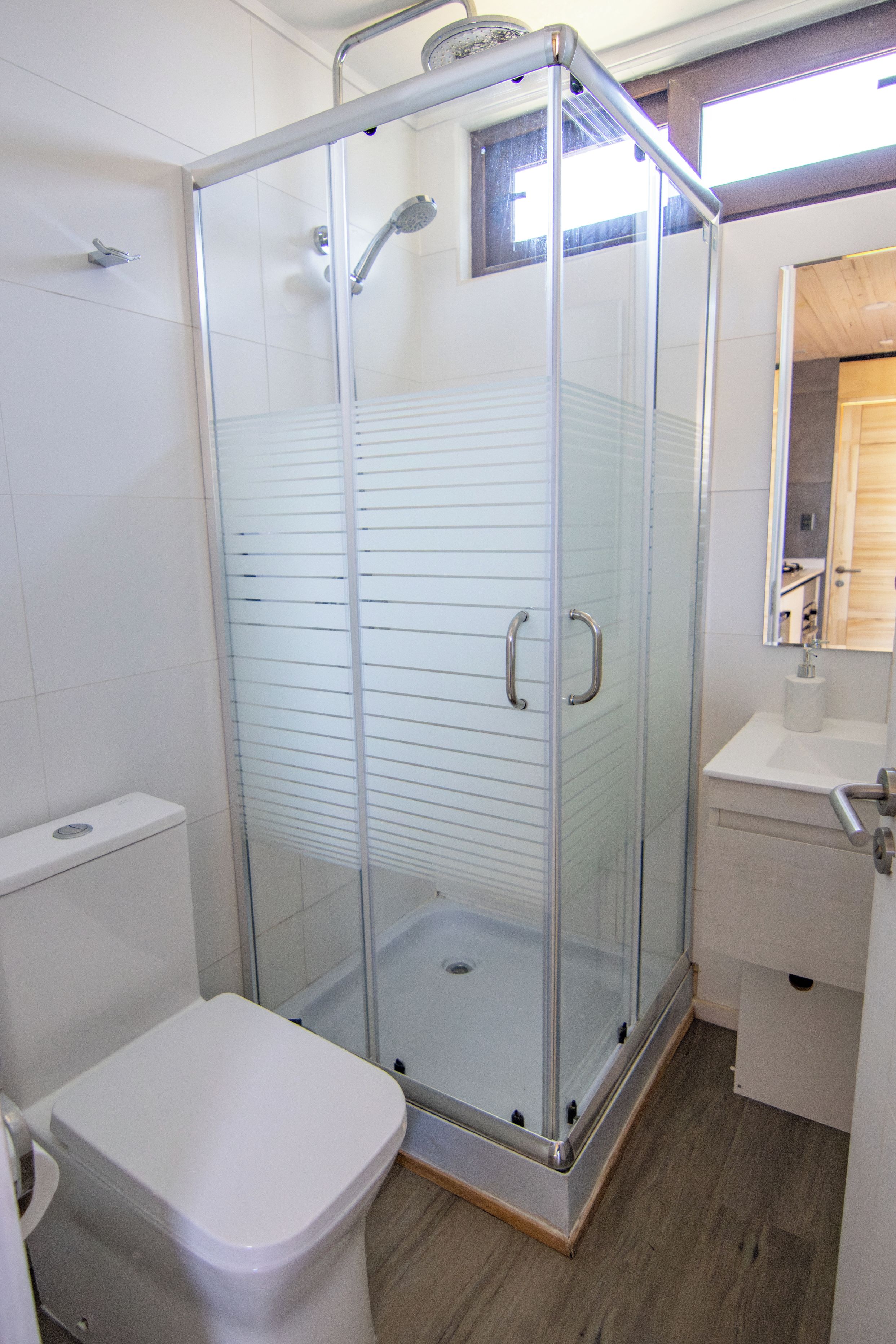 Cabina de ducha con paredes de cristal, un inodoro y un lavamanos blancos a la izquierda.
