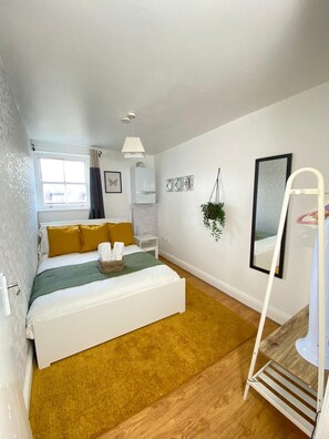 Une chambre à coucher avec un lit, une fenêtre, une armoire blanche, un miroir et une plante.
