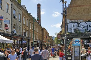 A busy street with people walking, shops, and a tall chimney. - Luxury Brick Lane Flat | Sleep 6 (London)