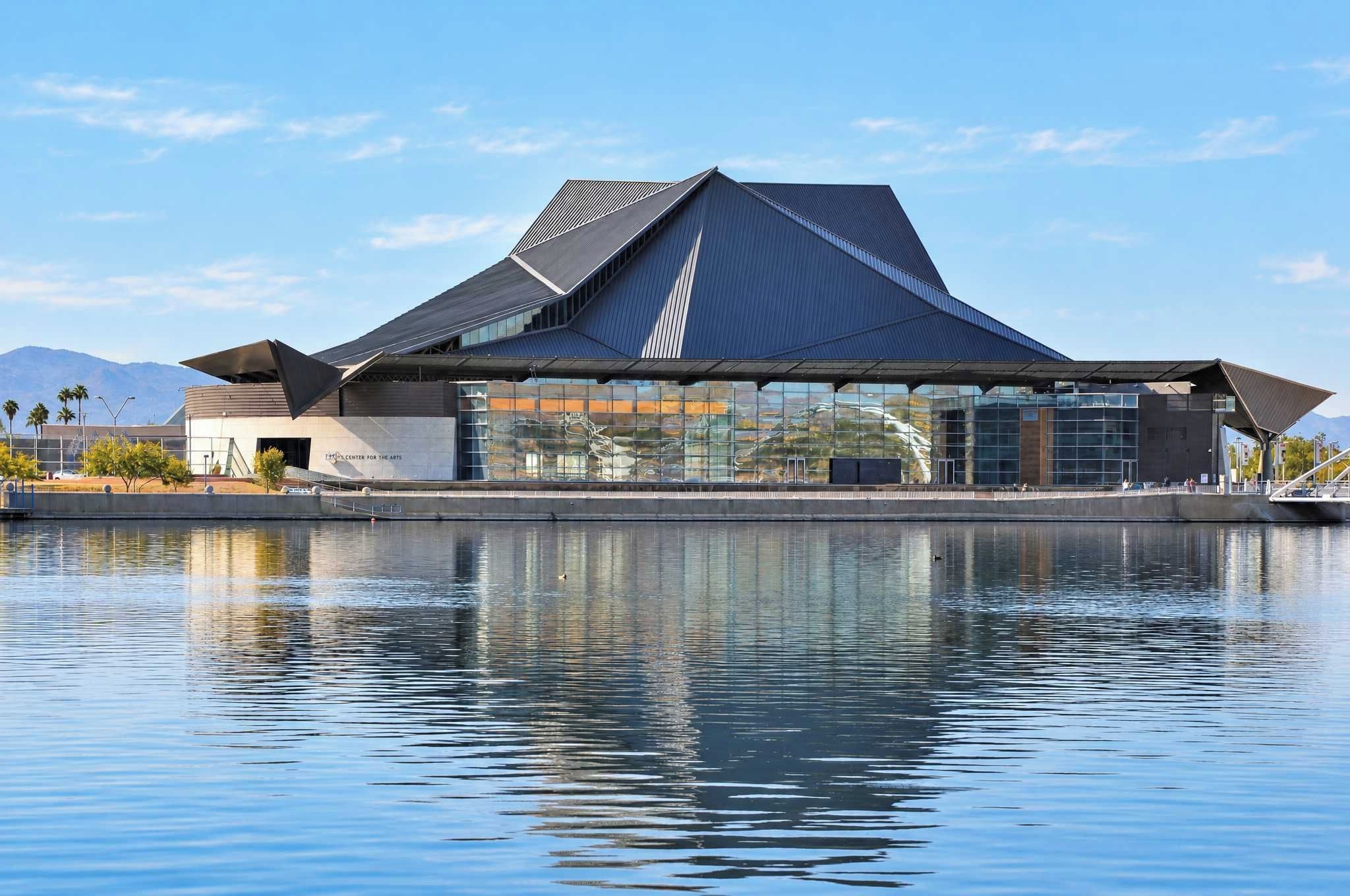 A modern building with a unique roof design, situated by a calm body of water.