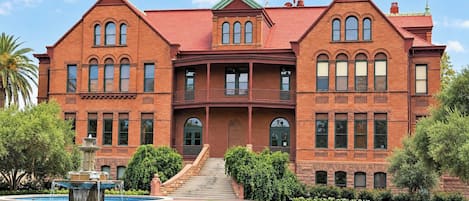 A large, two-story brick building with a symmetrical facade, a central entrance with a staircase, and a small fountain in the front courtyard.