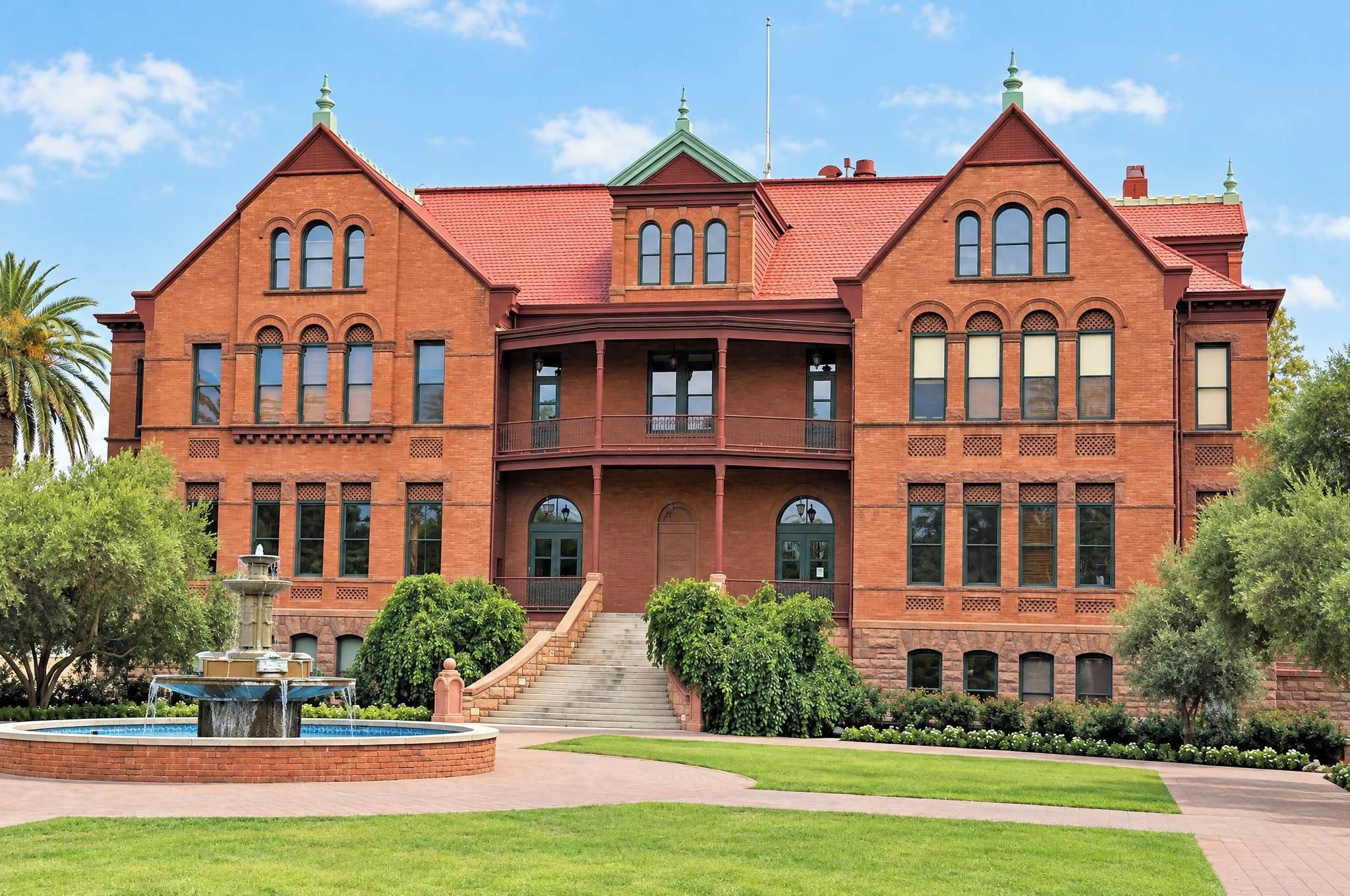 A large, two-story brick building with a symmetrical facade, a central entrance with a staircase, and a small fountain in the front courtyard.