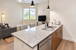 A modern kitchen with a granite countertop, stainless steel appliances, and a dining area with a gray sofa and chairs. - Boulevard Stays Modern Tempe 2BR ASU Pool, Gym (Tempe)