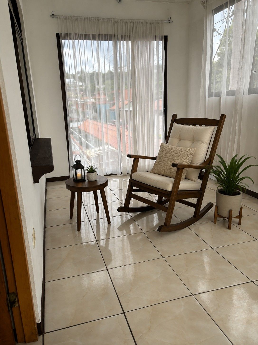 Ein Zimmer mit einem Schaukelstuhl, einem kleinen Tisch mit Kerze und einem Blumentopf.