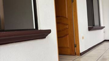 A hallway with a wooden door, a window, and a tiled floor.