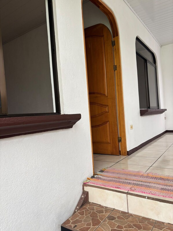 Un pasillo con puerta de madera, ventana y suelo de baldosas.