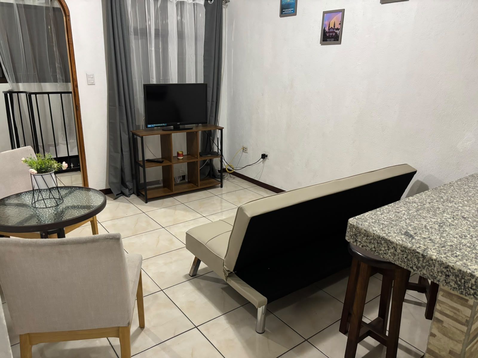 Ein Wohnzimmer mit Fernseher auf einem Holzboden, einer Couch, einem Esstisch und einer kleinen Topfpflanze.