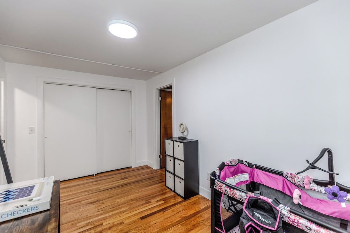 Una stanza con pavimento in legno, una porta bianca, un mobile contenitore nero e un passeggino con dettagli rosa.