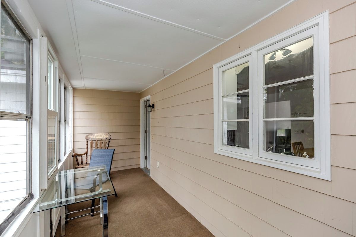 A corridor with beige siding walls, a glass table with chairs, and a window with a view.