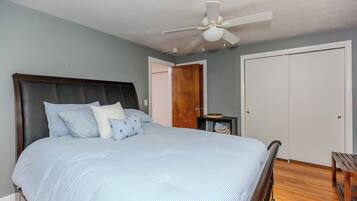 A bedroom with a bed, a ceiling fan, a wardrobe, and a small table.
