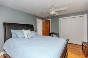 A bedroom with a bed, a ceiling fan, a wardrobe, and a small table.