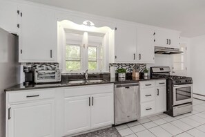 A modern kitchen with white cabinets, a built-in oven, a dishwasher, and a window above the sink.