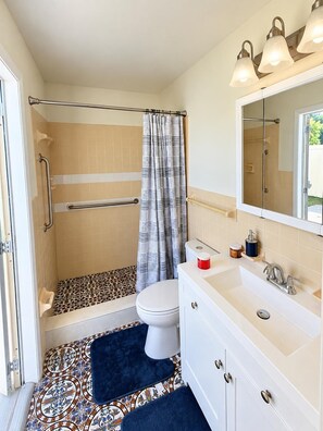 Een badkamer met een douche, toilet en wastafel, met een vloer met een patroon en een blauwe badmat.