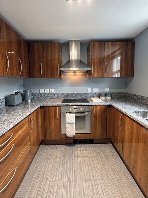 A modern kitchen with wooden cabinets, a stainless steel range hood, and a granite countertop. - Stylish Central Lytham 2 Bed - Walk Everywhere (Lytham Saint Annes)