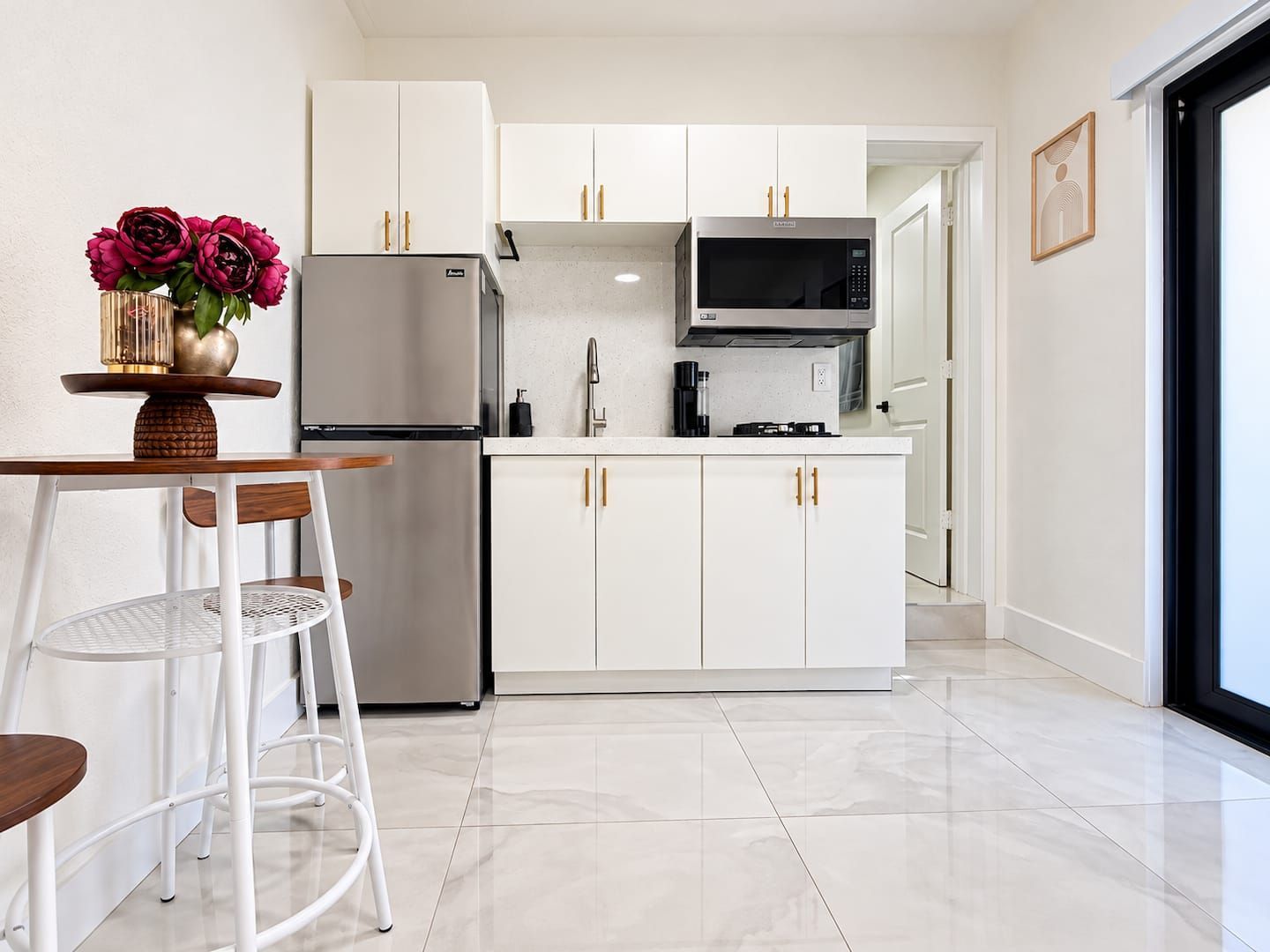 Una cucina moderna con mobili bianchi, un frigorifero in acciaio inossidabile, un forno a microonde e un'area pranzo con tavolo e sedie.