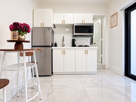Uma cozinha moderna com armários brancos, geladeira de aço inoxidável, micro-ondas e uma área de jantar com mesa e cadeiras.