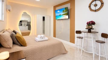 Una habitación de hotel moderna con una cama, televisor, zona de comedor con sillas y un reloj fijado a la pared.