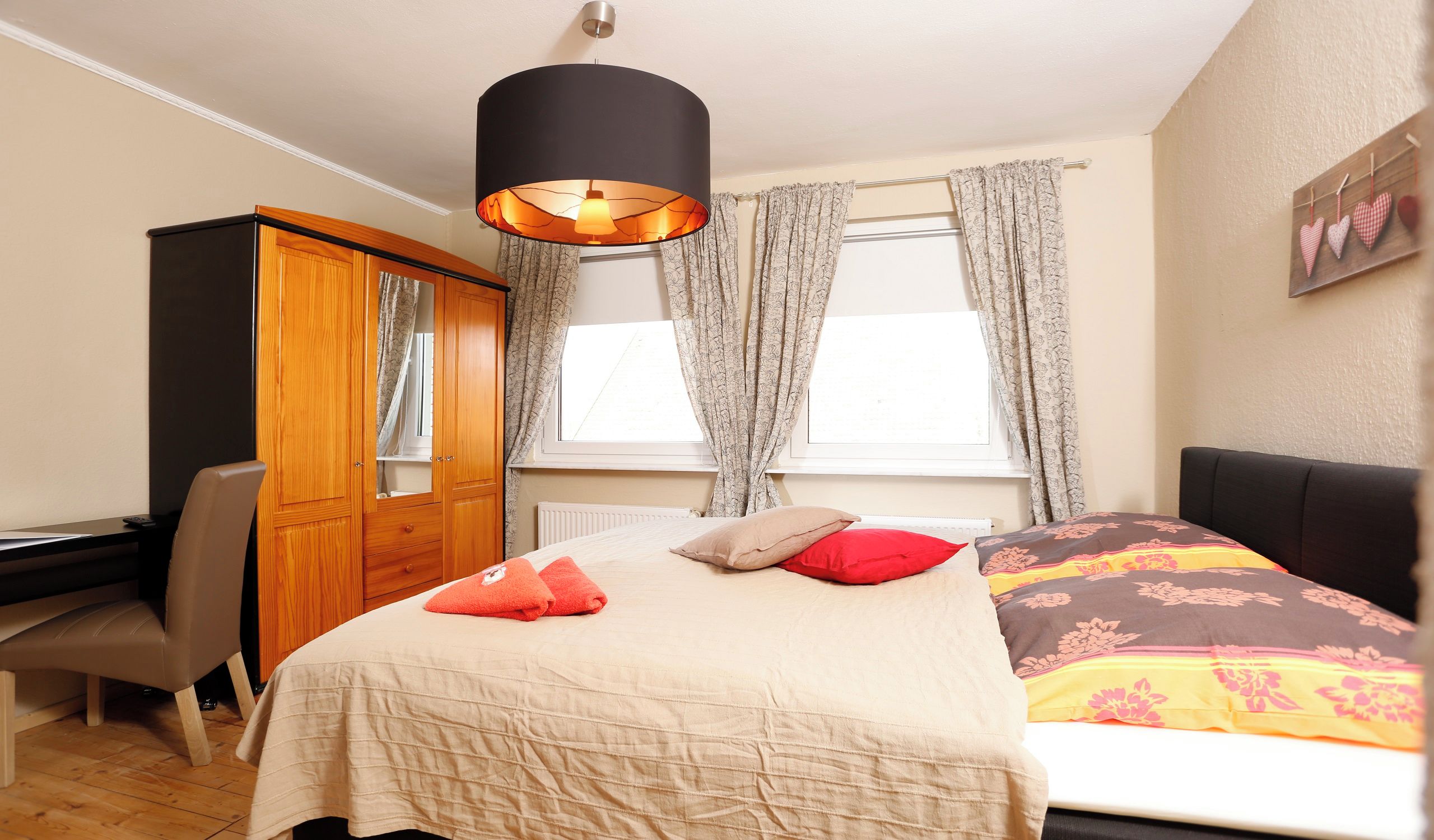 Ein Schlafzimmer mit einem Bett, einem Schreibtisch, einem Kleiderschrank und einem Fenster mit Vorhängen.