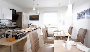 A modern kitchen with a dining area, including a breakfast bar, seating, and a television.