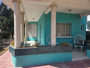 A building with a teal facade, large columns, a covered porch, and a decorative chair. - Spacious home available for Day of the Dead! (Oaxaca de Juárez)