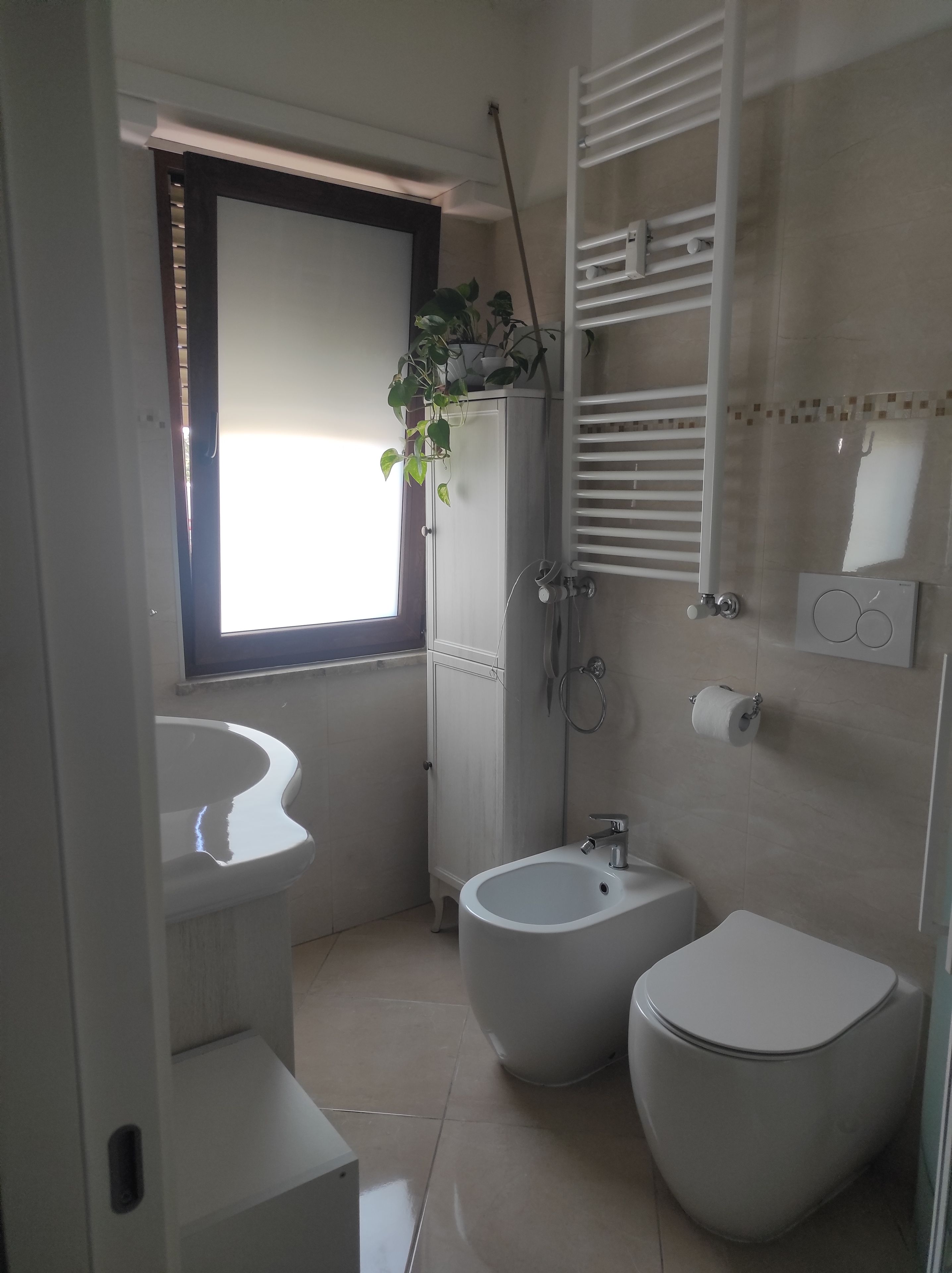 A modern bathroom with a sink, bidet, toilet, and a window with blinds.