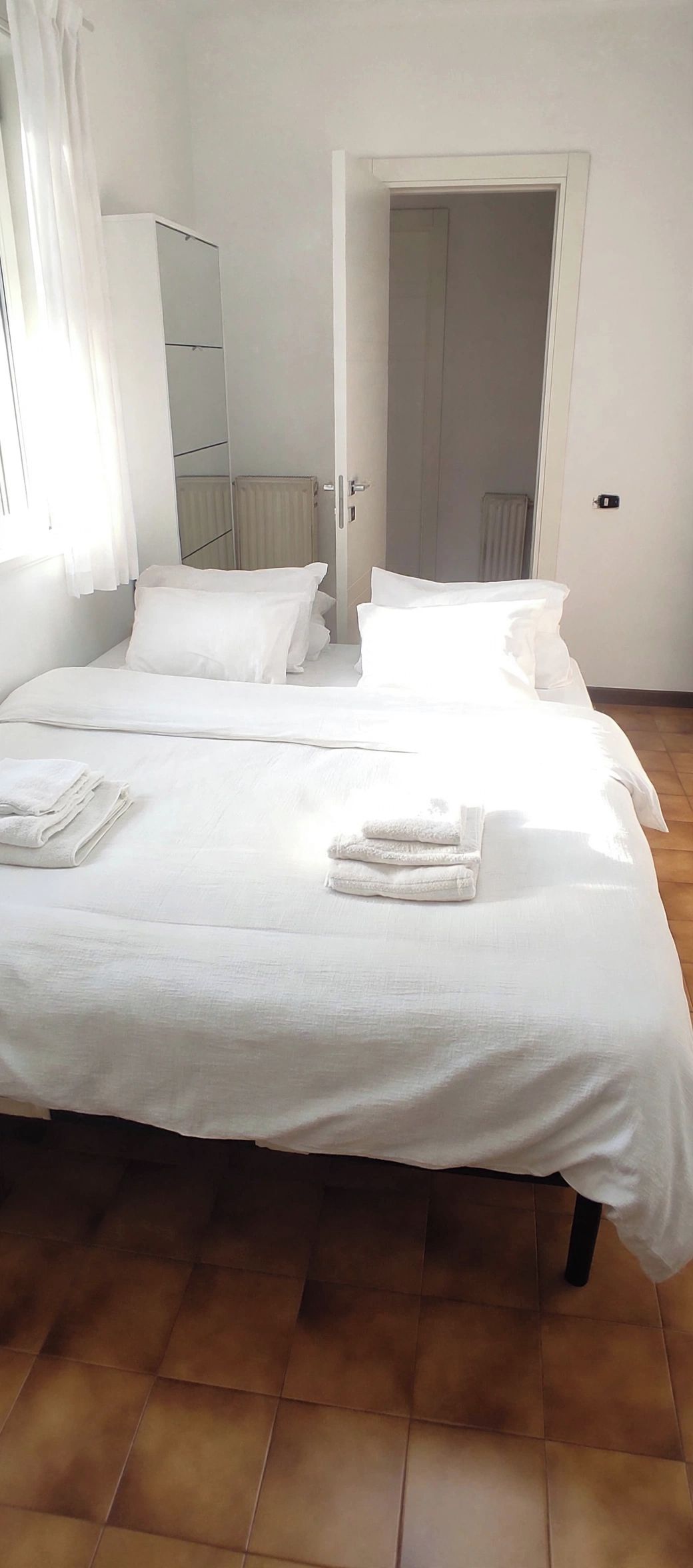A hotel room with a bed, a window with curtains, a door, and a radiator.