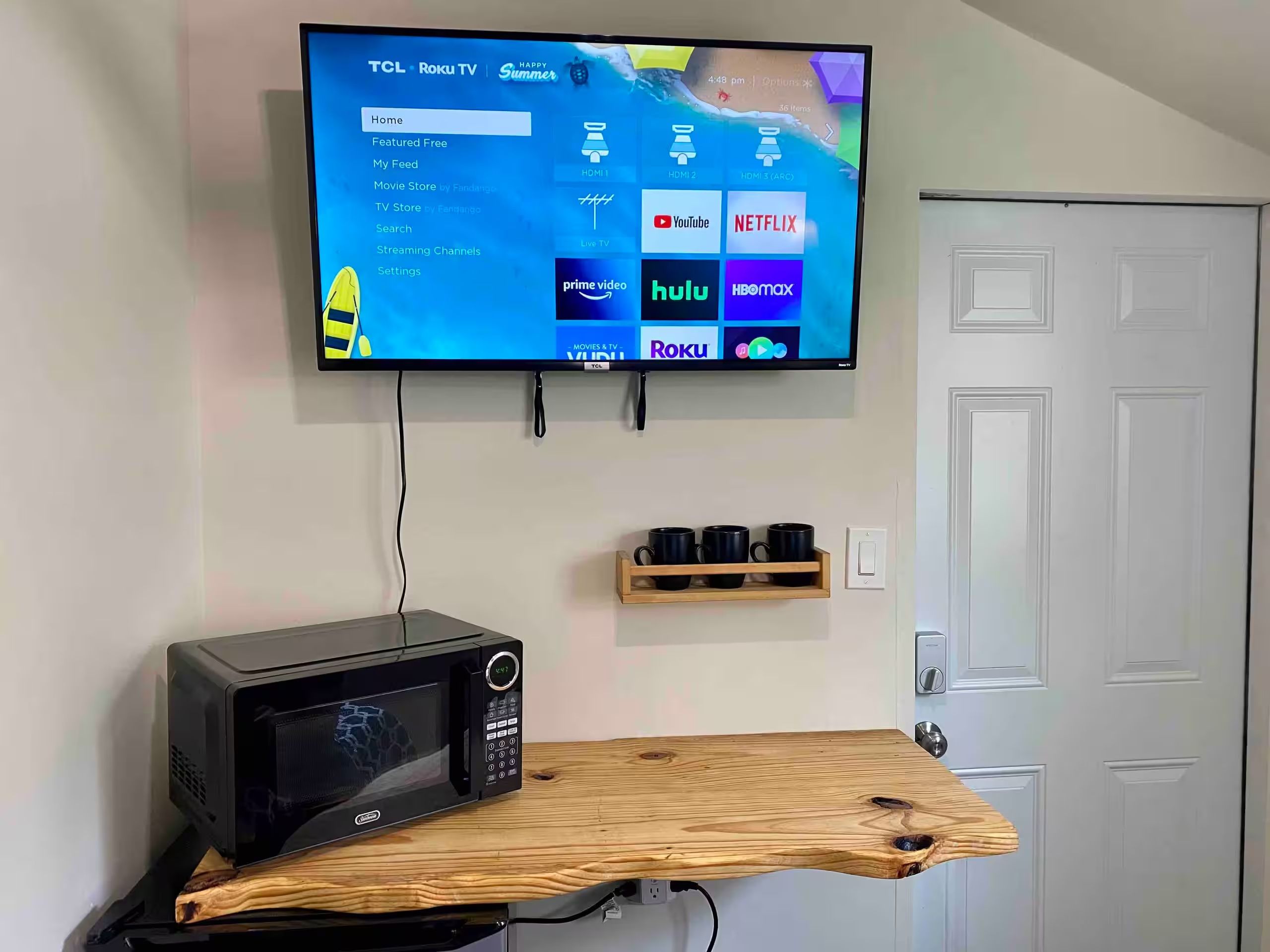 Un televisor TCL Roku montado en una pared con un estante de madera debajo.