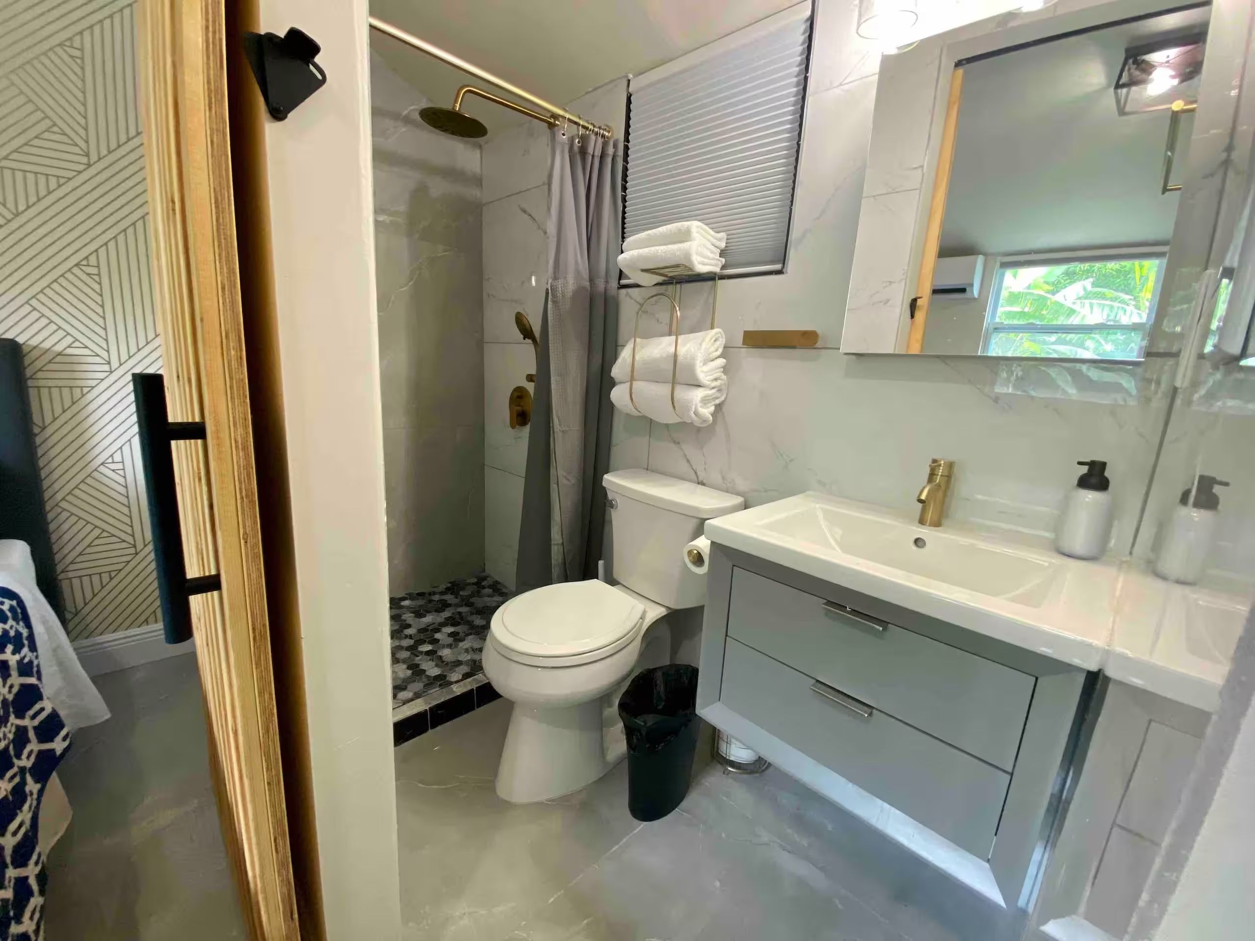 A bathroom with a shower, toilet, sink, and a mirror.