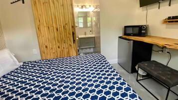 A bedroom with a bed, a desk, a television, and a bathroom visible through a sliding door.